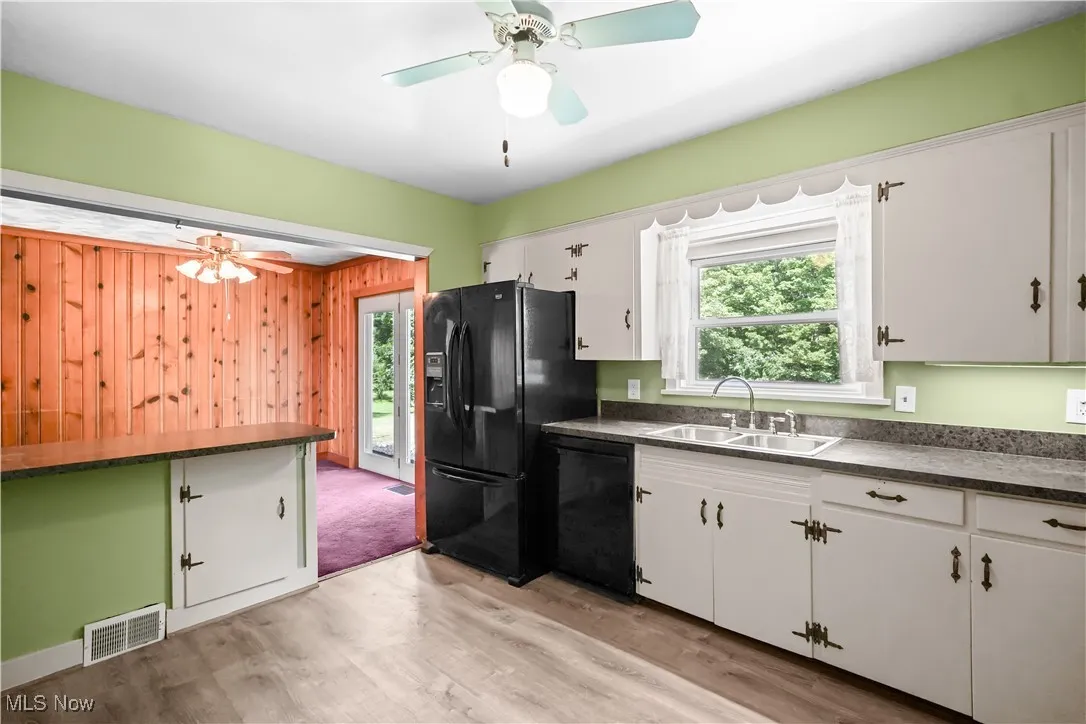 Kitchen featuring dark countertops, light wood finished floors, white cabinetry, dishwasher, and wood walls