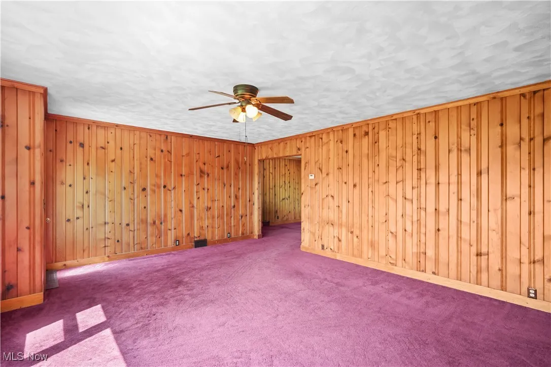 Carpeted spare room featuring a ceiling fan and wood walls