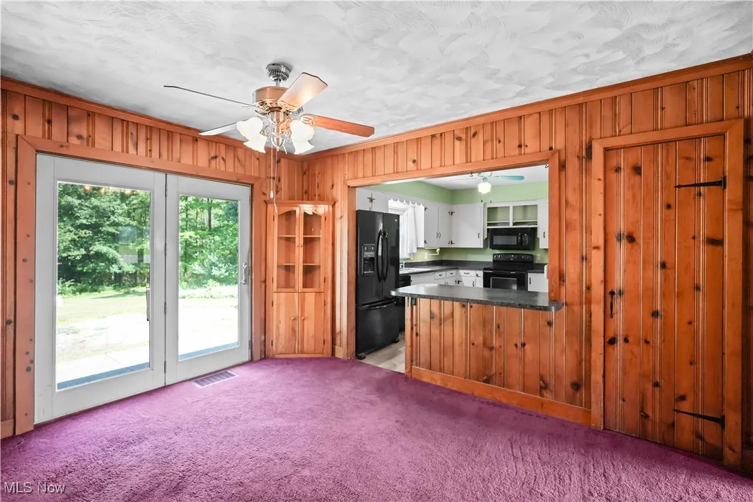 Kitchen with a ceiling fan, wood walls, dark countertops, black appliances, and light colored carpet