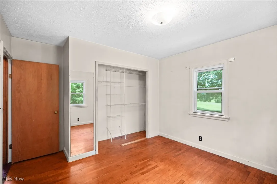 Unfurnished bedroom with a closet, wood-type flooring, multiple windows, and a textured ceiling