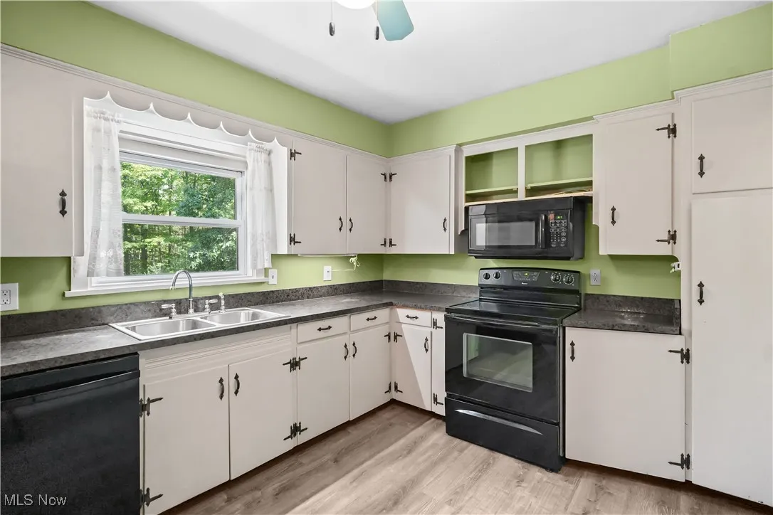 Kitchen with black appliances, white cabinetry, dark countertops, a ceiling fan, and light wood-type flooring