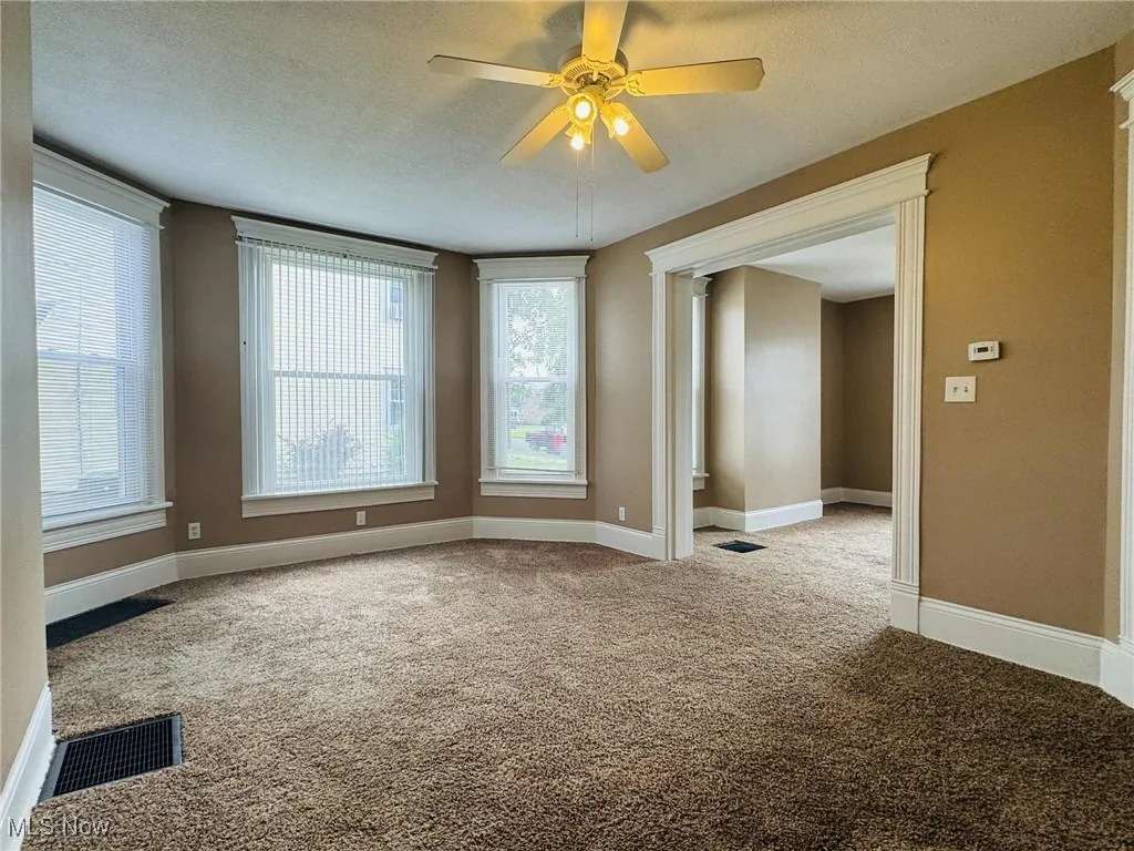 Carpeted empty room with a ceiling fan, plenty of natural light, and a textured ceiling