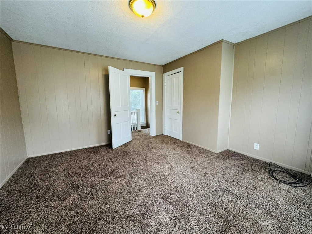 Carpeted empty room featuring a textured ceiling and wood walls