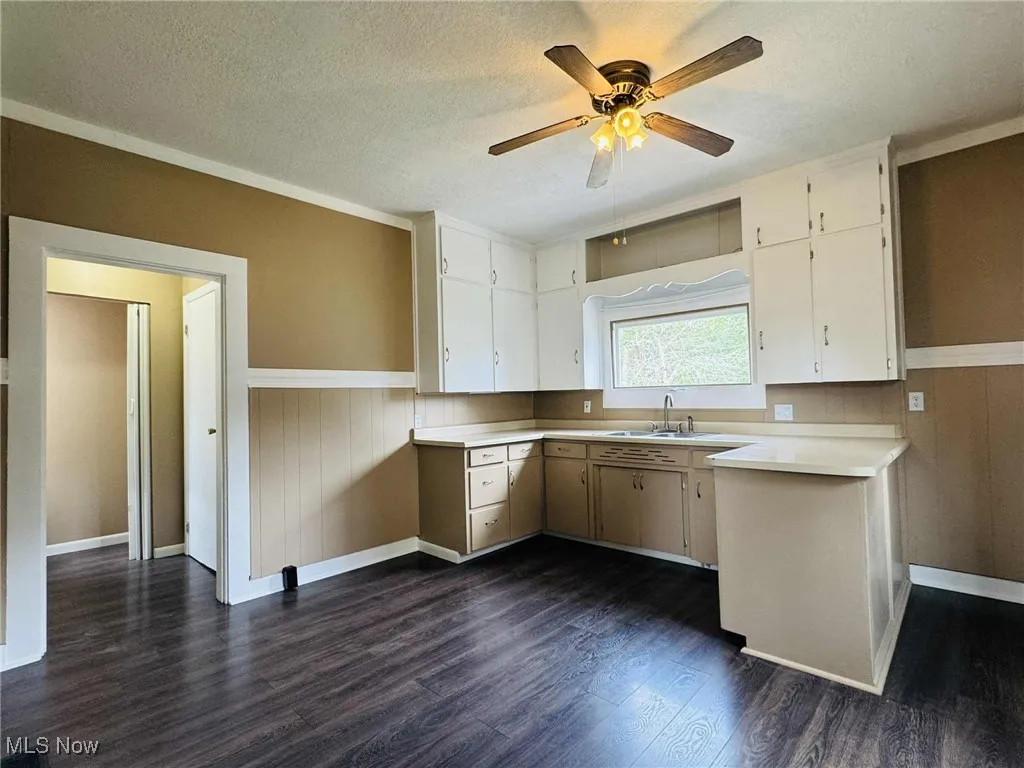 Kitchen featuring dark wood finished floors, light countertops, ceiling fan, a wainscoted wall, and white cabinetry