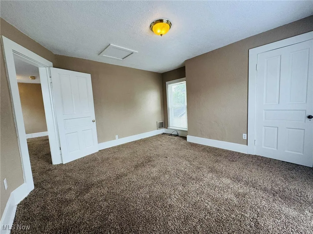 Unfurnished bedroom with carpet floors, a textured ceiling, and attic access