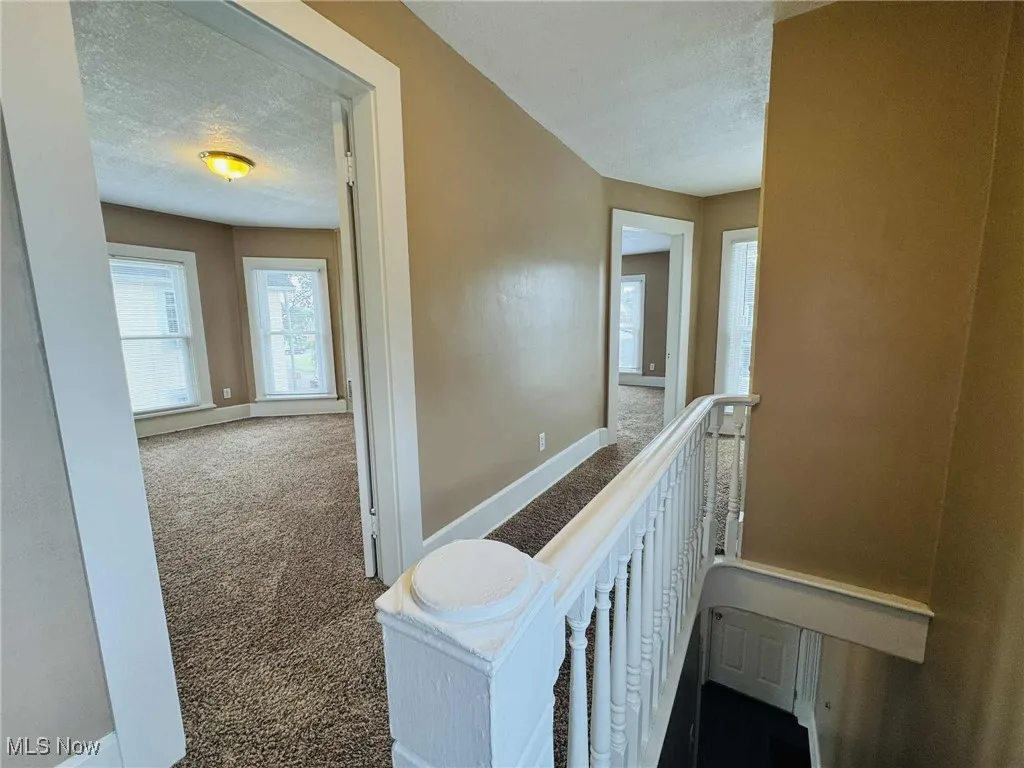 Hallway featuring carpet, a textured ceiling, and an upstairs landing