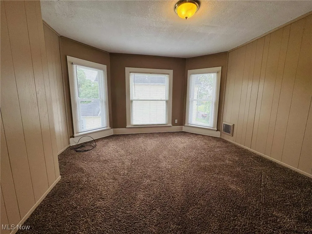 Carpeted spare room with a textured ceiling and wood walls