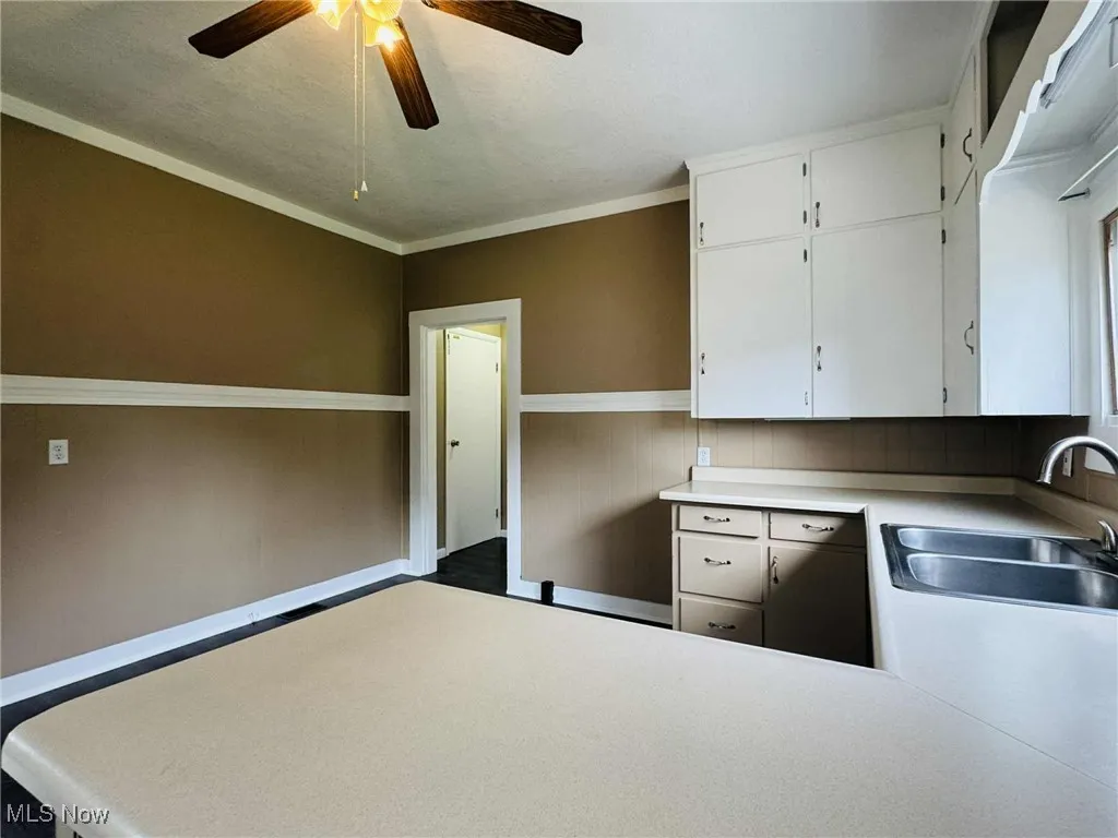 Kitchen with a ceiling fan, white cabinets, light countertops, and crown molding