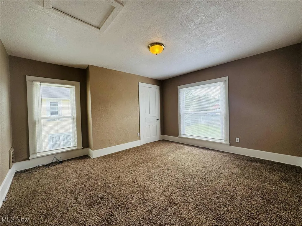 Unfurnished room with a textured ceiling, carpet floors, healthy amount of natural light, and attic access