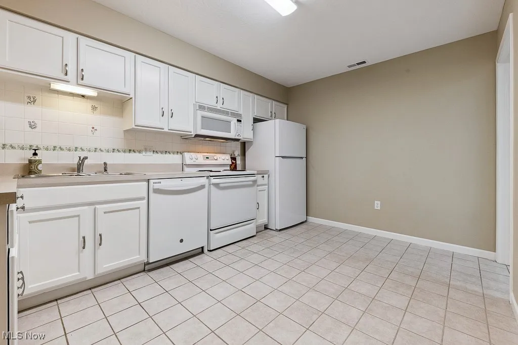 Kitchen featuring white appliances, light countertops, decorative backsplash, and white cabinetry