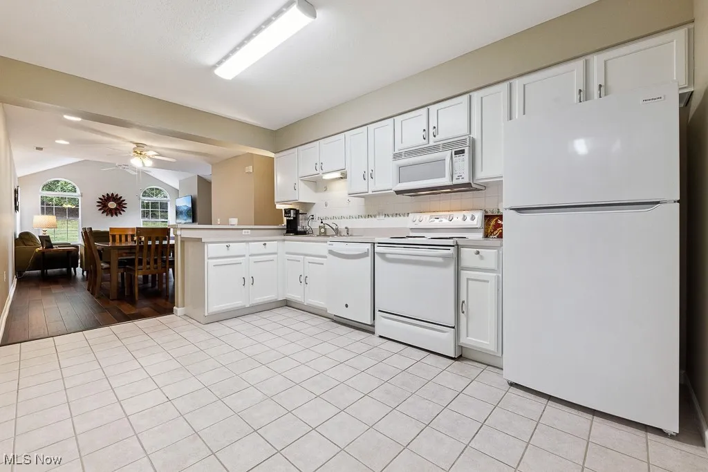 Kitchen featuring white appliances, a peninsula, ceiling fan, white cabinets, and vaulted ceiling