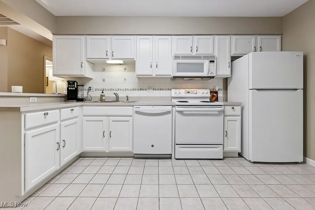 Kitchen featuring white appliances, white cabinets, tasteful backsplash, and light tile patterned flooring