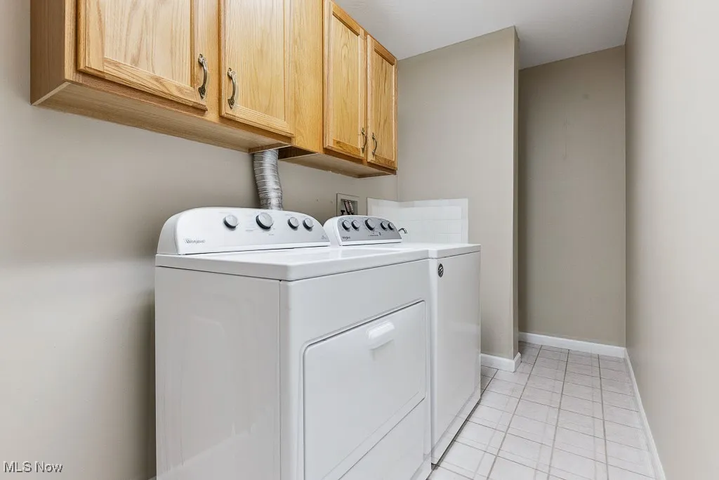 Washroom with washer and clothes dryer, cabinet space, and light tile patterned floors