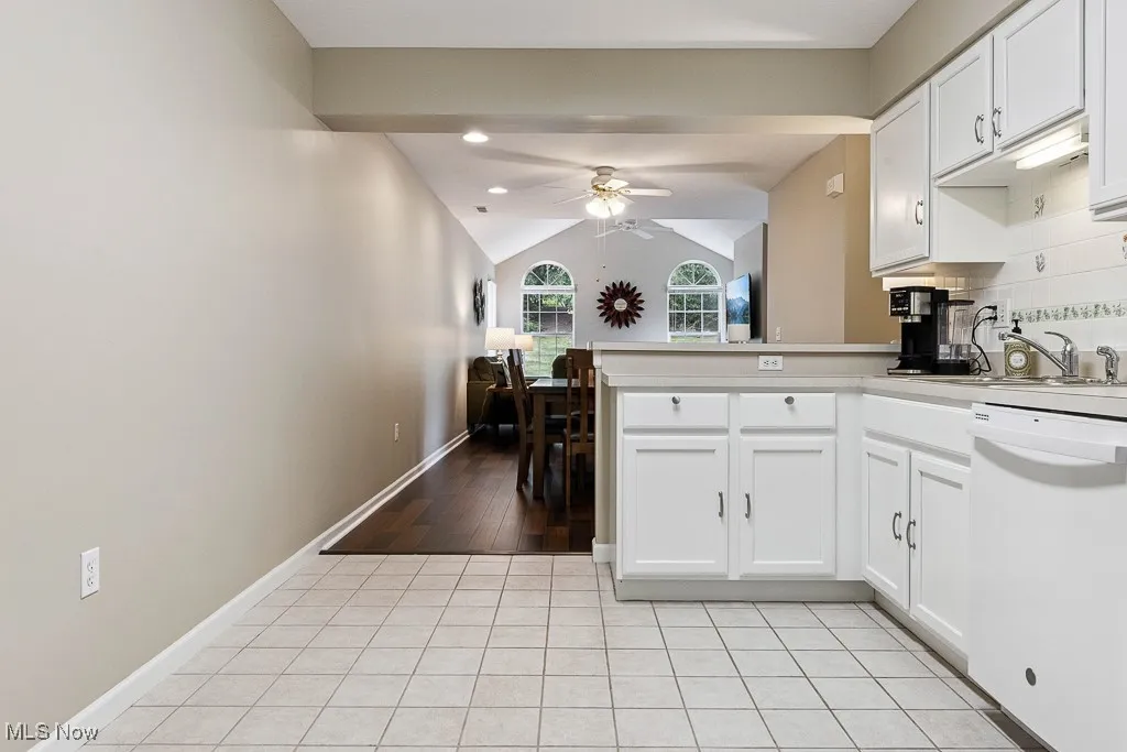 Kitchen featuring white dishwasher, ceiling fan, a peninsula, white cabinets, and lofted ceiling
