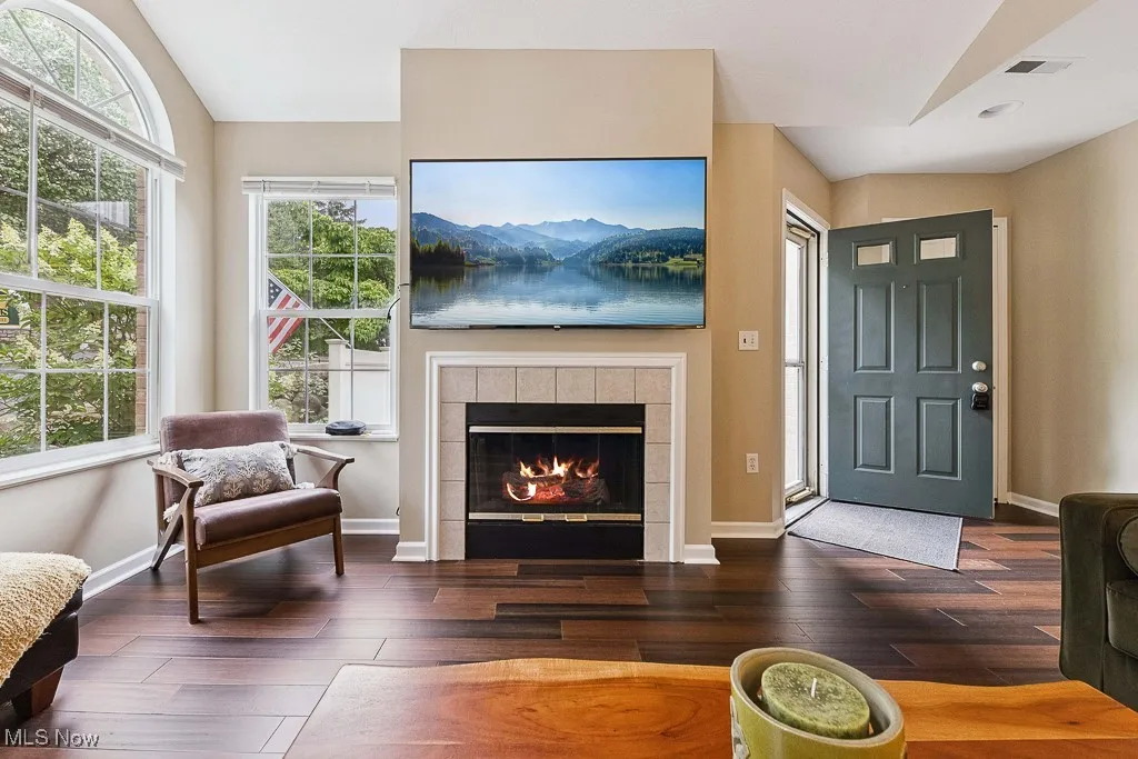 Living Room with lofted ceiling, healthy amount of natural light, wood finished floors, and a tiled fireplace