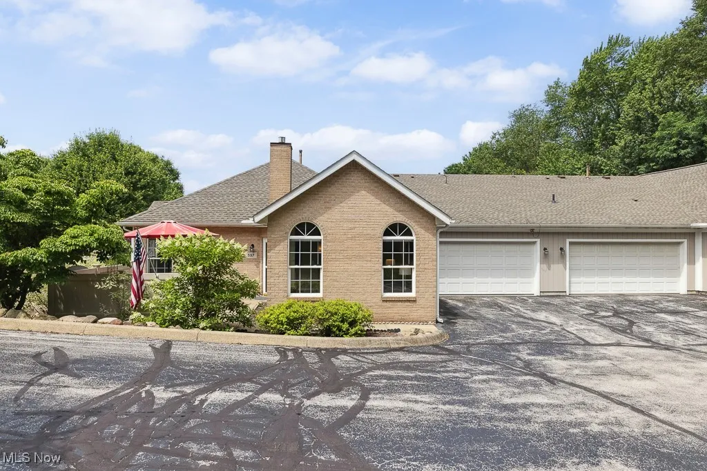 View of front of property with driveway, a shingled roof, a garage, a chimney, and brick siding