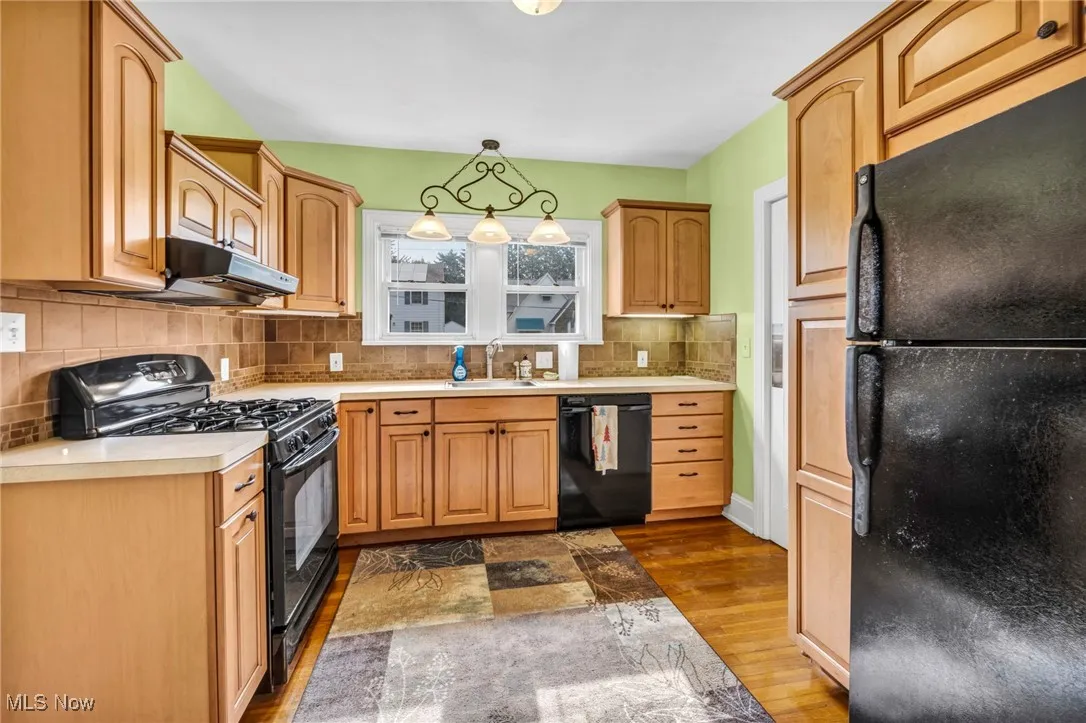 Kitchen with black appliances, dark wood-style flooring, light countertops, decorative backsplash, and pendant lighting