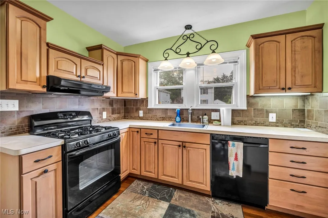 Kitchen with black appliances, under cabinet range hood, light countertops, dark wood-type flooring, and decorative backsplash