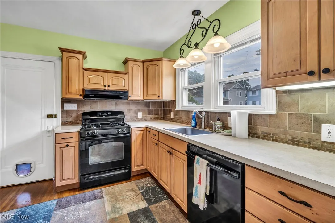 Kitchen featuring black appliances, light countertops, under cabinet range hood, and backsplash