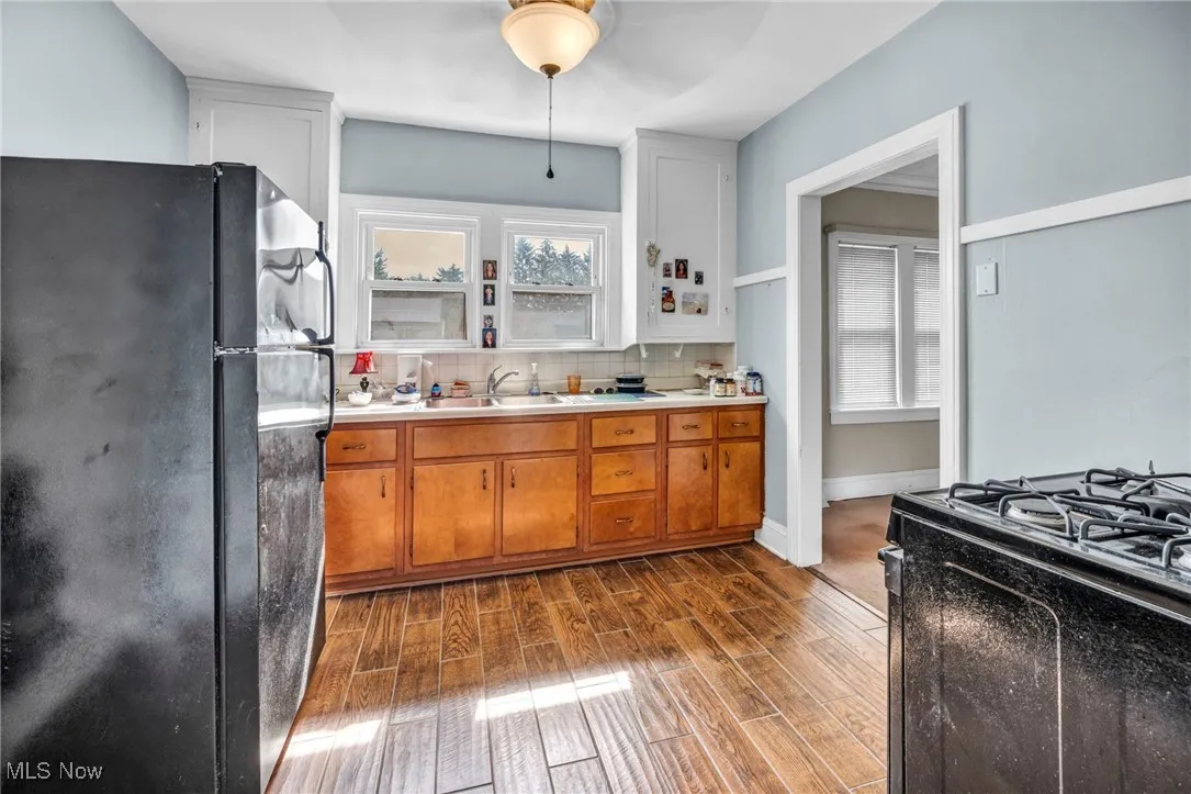 Kitchen featuring black appliances, brown cabinetry, dark wood-style flooring, decorative backsplash, and light countertops