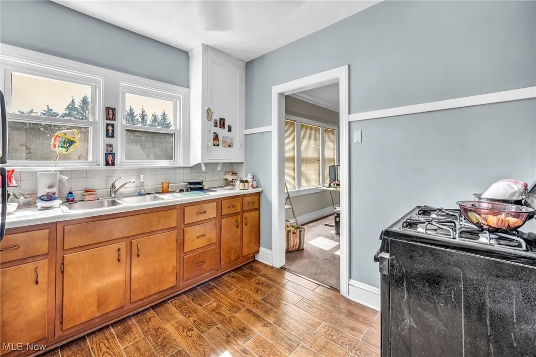 Kitchen featuring gas range, dark wood-type flooring, light countertops, backsplash, and brown cabinets