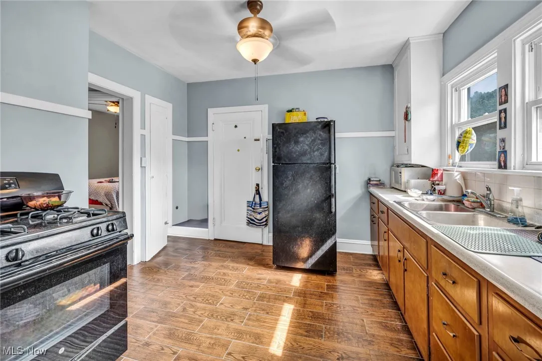Kitchen featuring black appliances, light countertops, wood finished floors, brown cabinets, and a ceiling fan