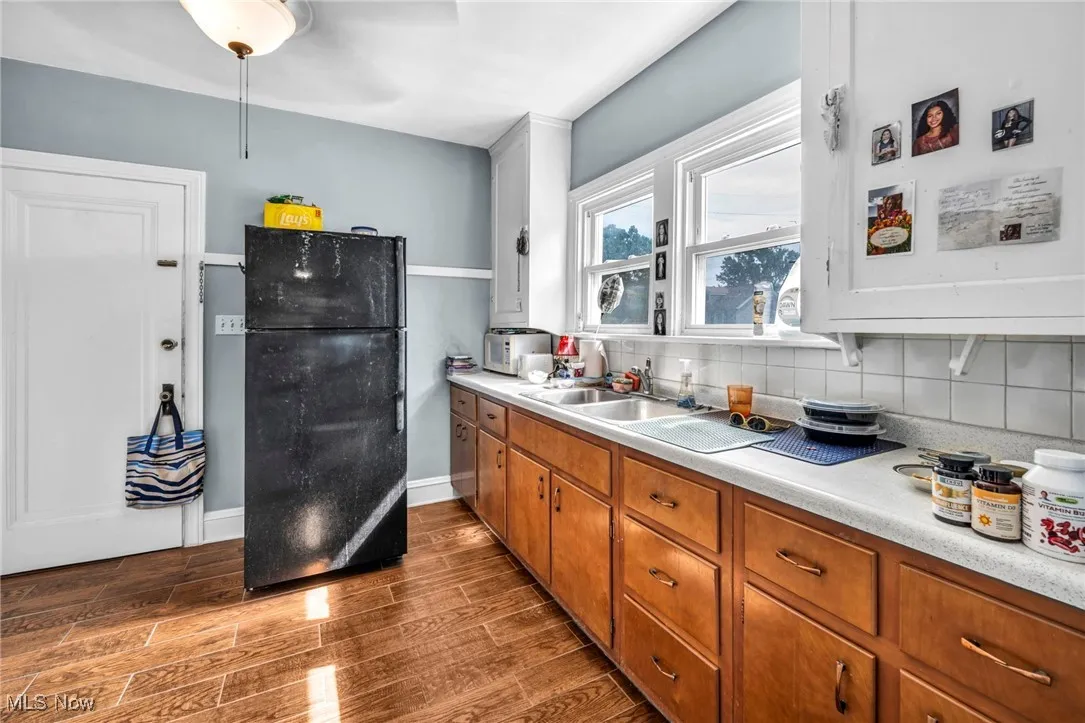Kitchen with freestanding refrigerator, light countertops, dark wood-style flooring, decorative backsplash, and brown cabinets