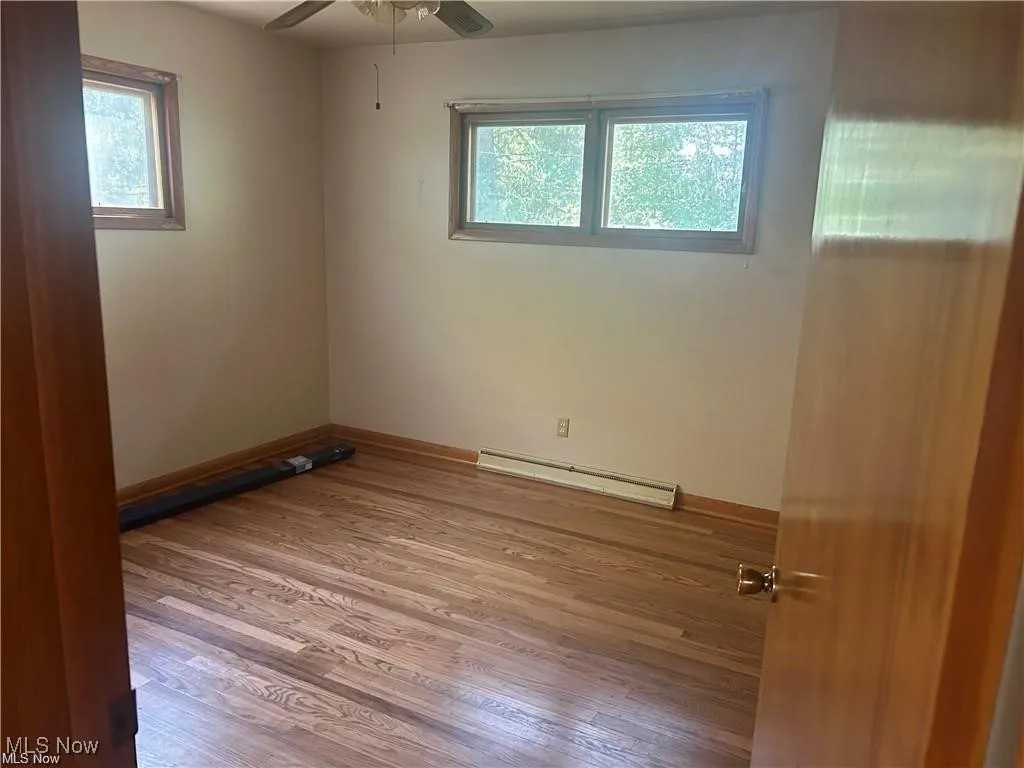 Unfurnished room with baseboard heating, wood finished floors, and a ceiling fan