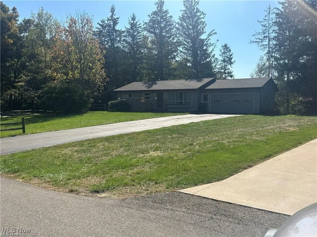 Ranch-style home featuring concrete driveway, an attached garage, and a front lawn