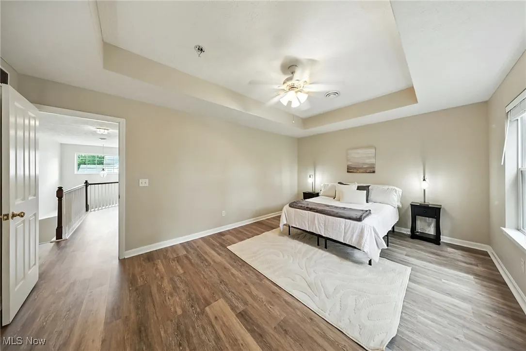 Bedroom featuring a raised ceiling, wood finished floors, and a ceiling fan