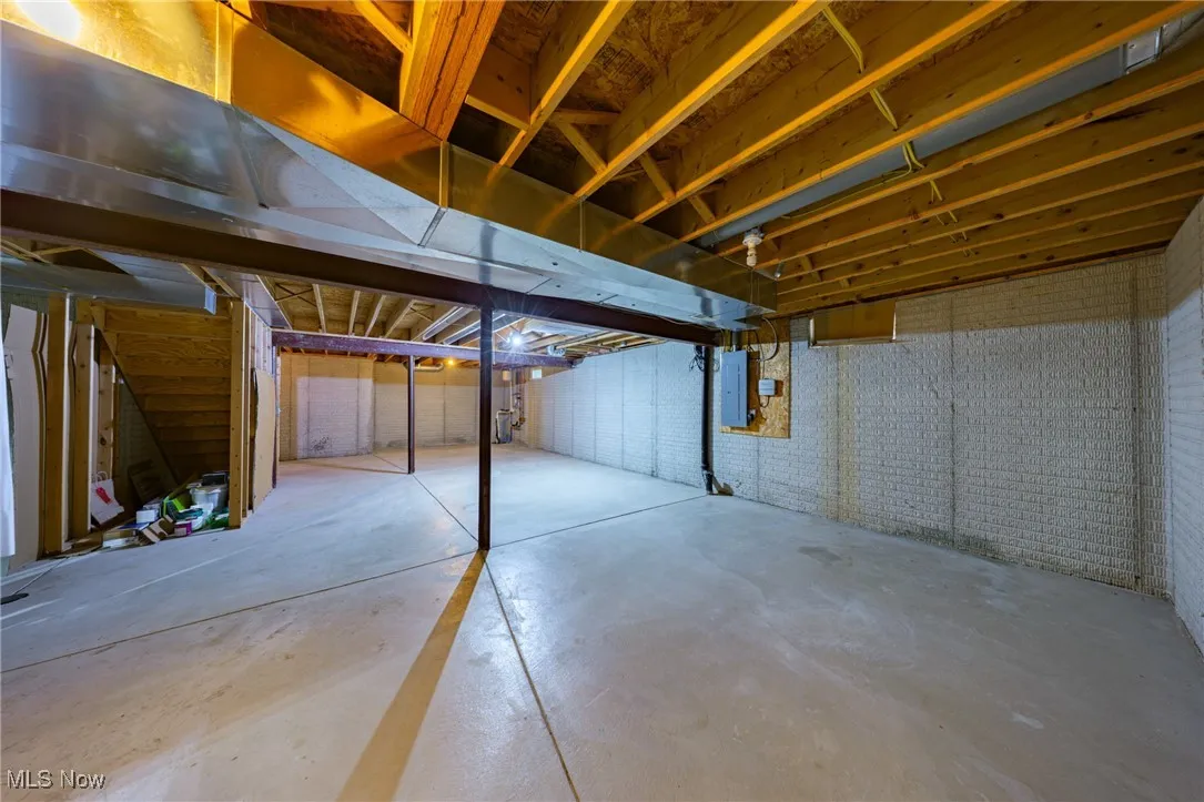 Unfinished basement with electric panel and brick wall