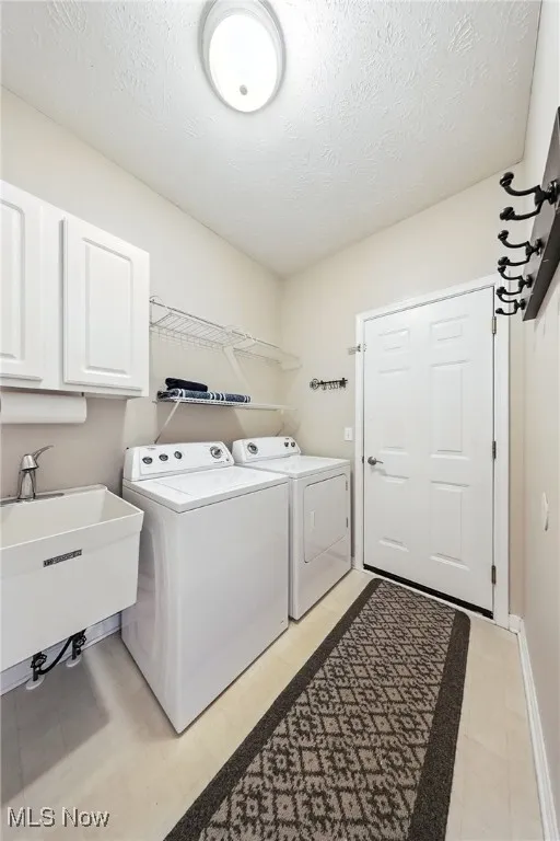 Laundry area featuring washer and clothes dryer, cabinet space, a textured ceiling, and light tile patterned flooring