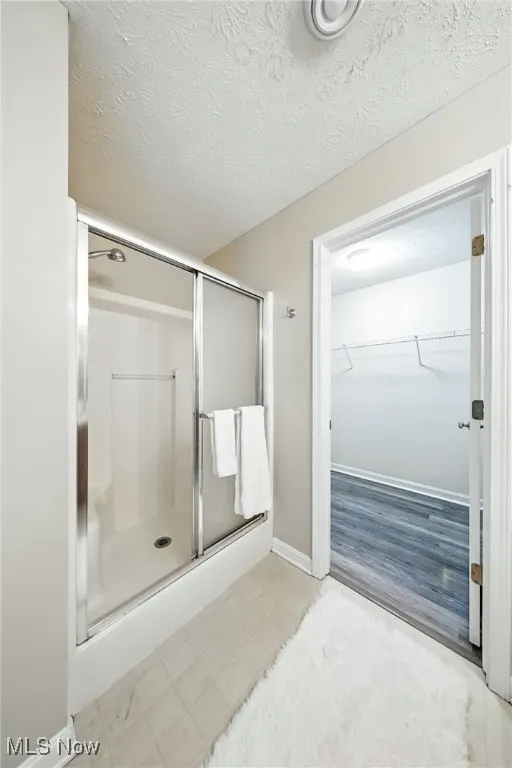 Bathroom featuring a stall shower, a spacious closet, and a textured​​‌​​​​‌​​‌‌​‌‌​​​‌‌​‌​‌​‌​​​‌​​ ceiling