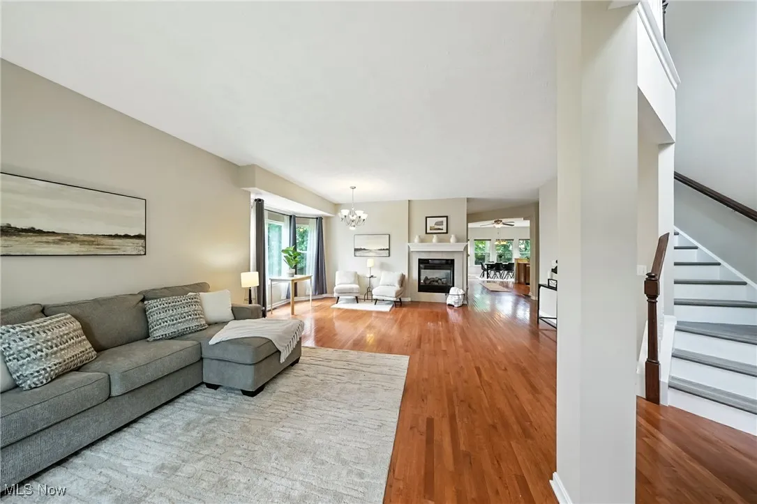Living room featuring wood finished floors, stairs, a chandelier, and a glass covered fireplace
