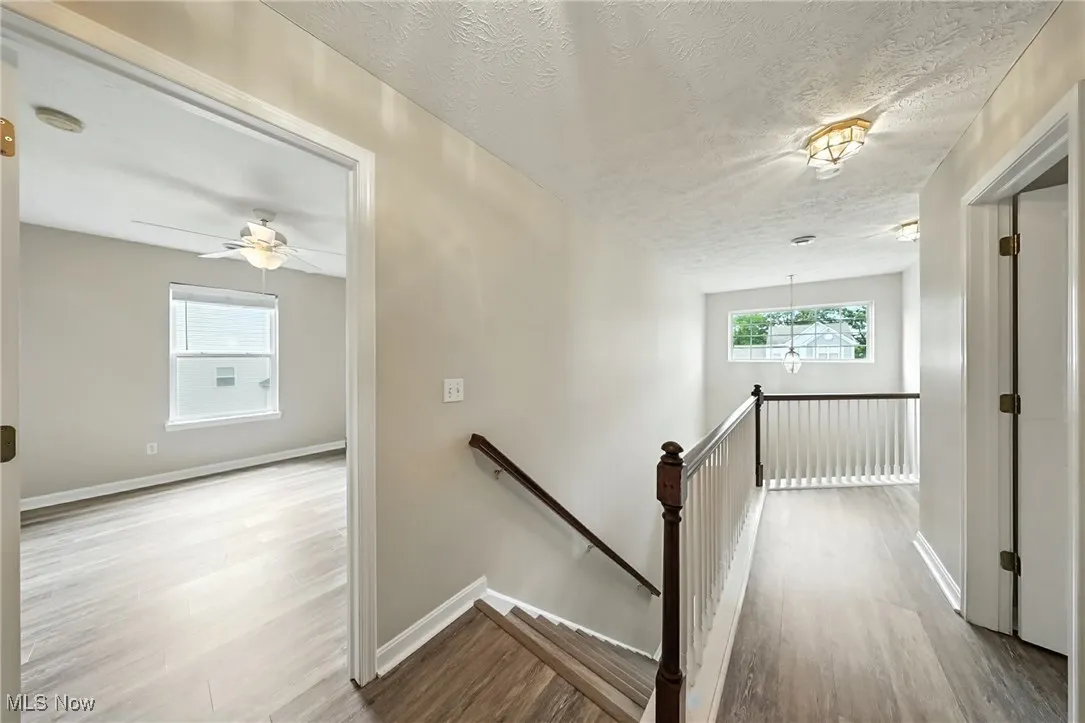 Hall featuring an upstairs landing, wood finished floors, and a textured ceiling