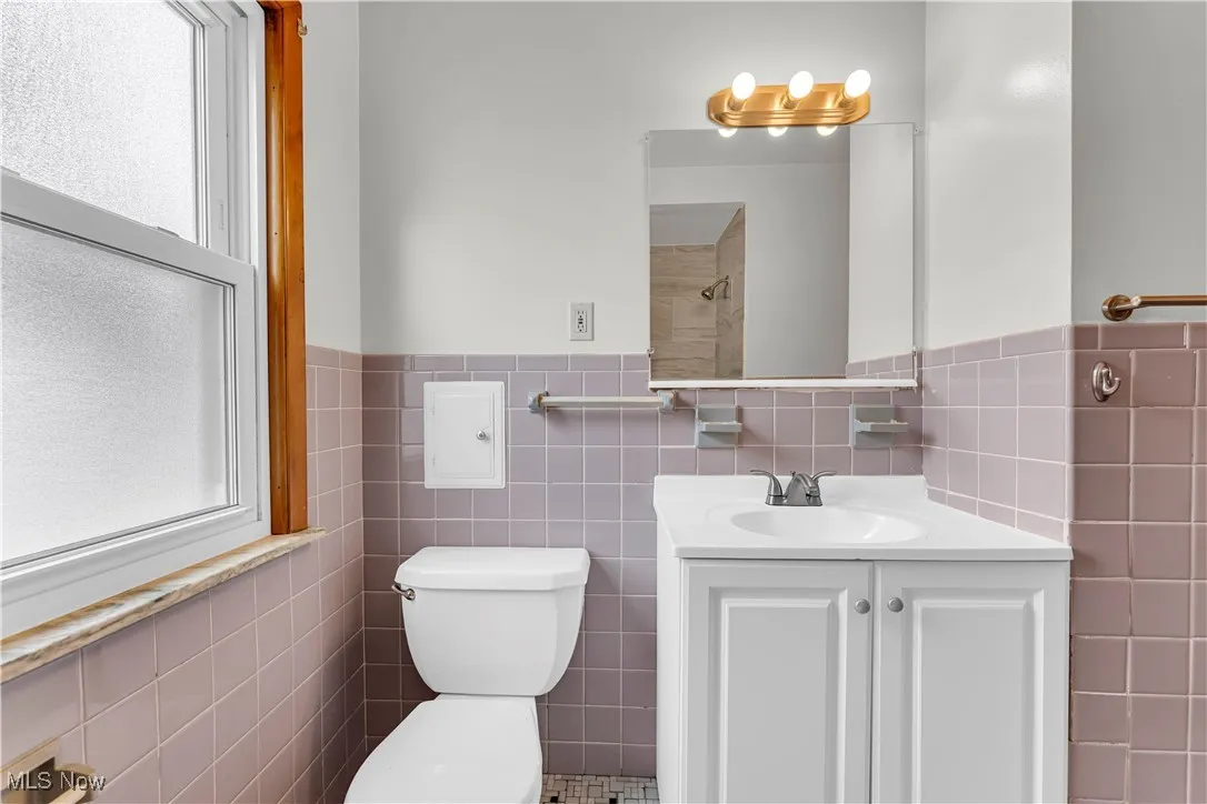 Full bathroom featuring tile walls, vanity, and a wainscoted wall