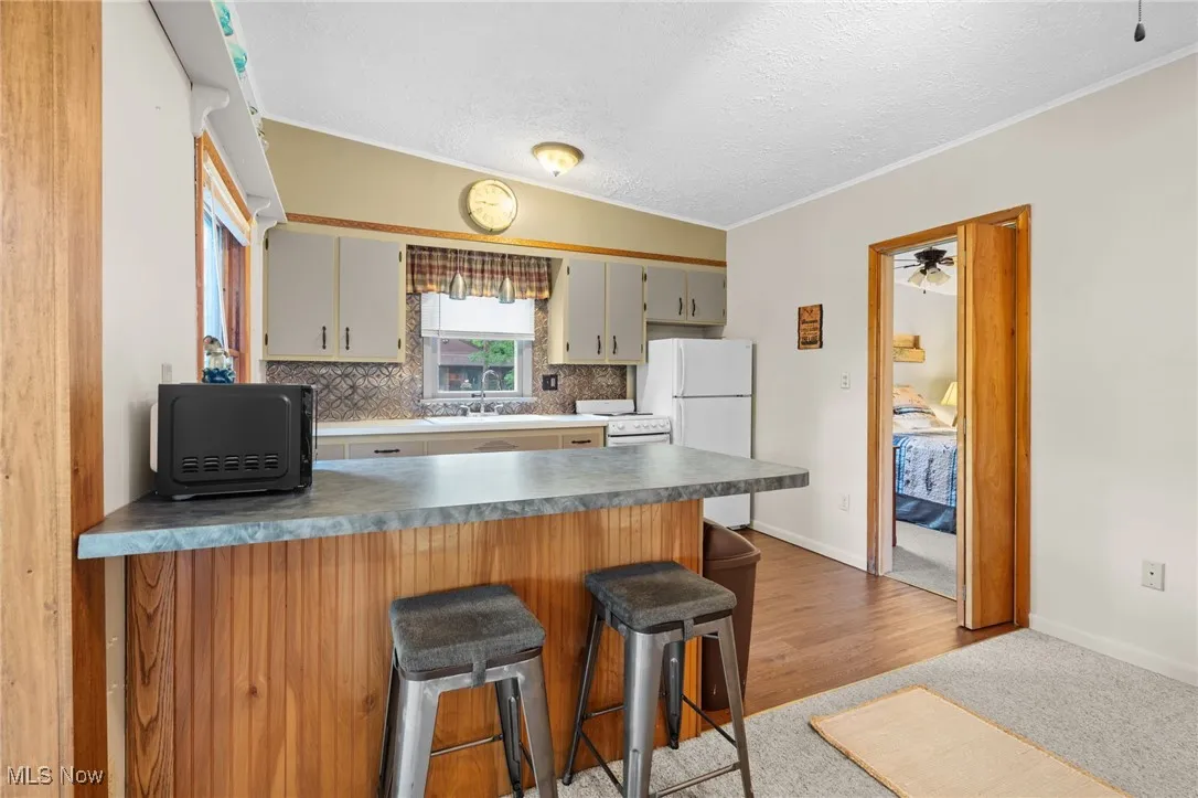 Kitchen featuring decorative backsplash, a peninsula, white appliances, a kitchen breakfast bar, and a textured ceiling