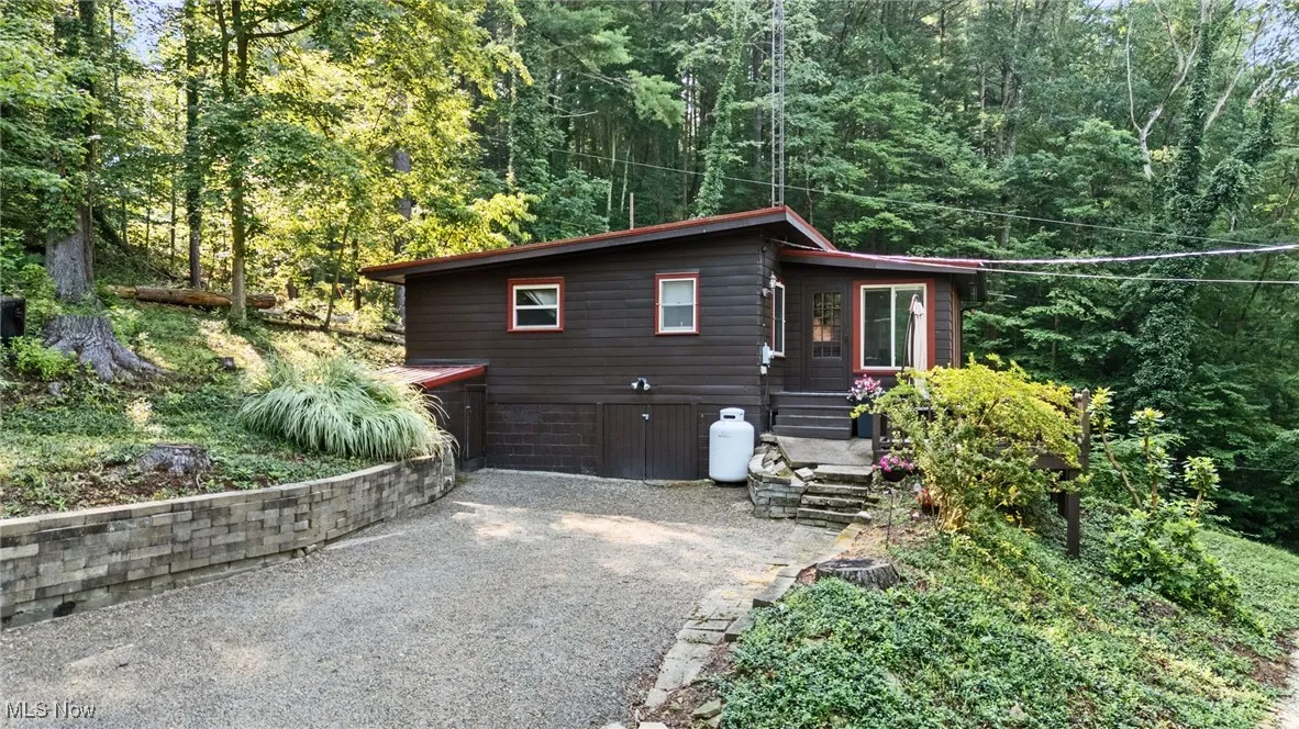 View of side of property with gravel driveway and a wooded view