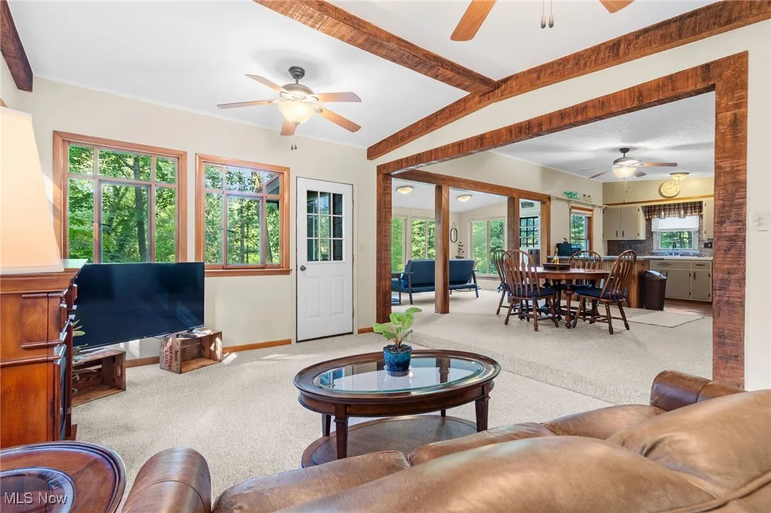 Living room featuring a ceiling fan, carpet floors, and beamed ceiling