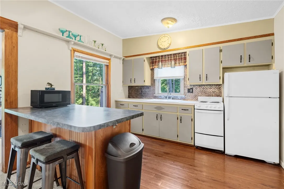 Kitchen with white appliances, decorative backsplash, a peninsula, wood finished floors, and a kitchen breakfast bar