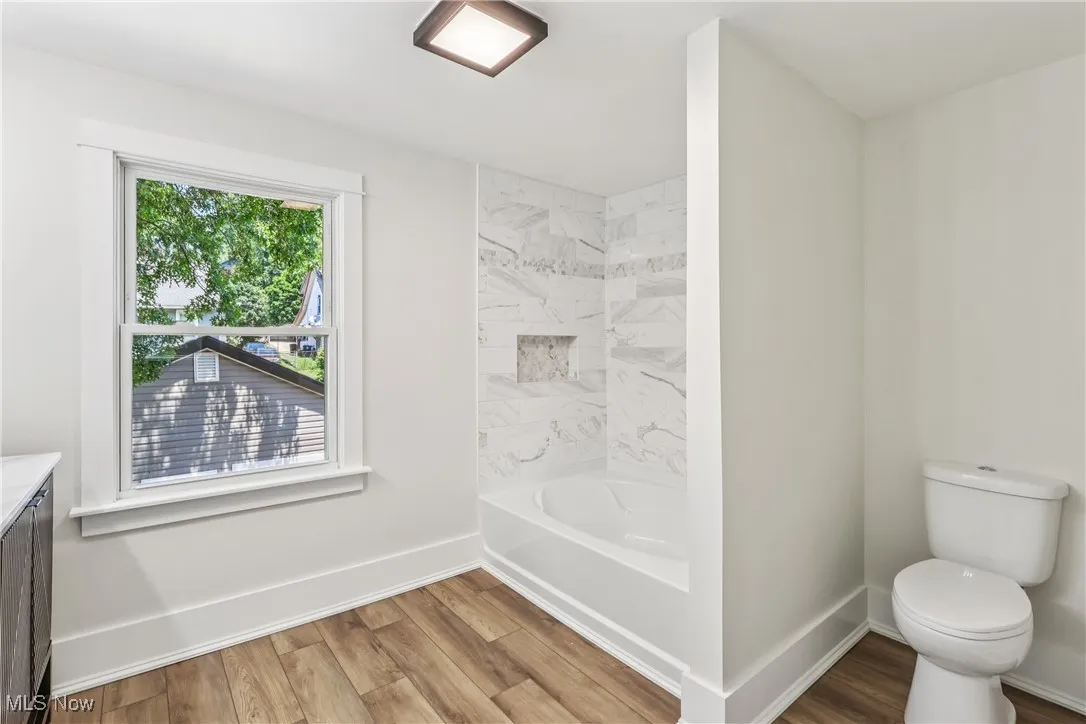 Bathroom with vanity, tiled shower / bathtub combo, commode and LVT flooring