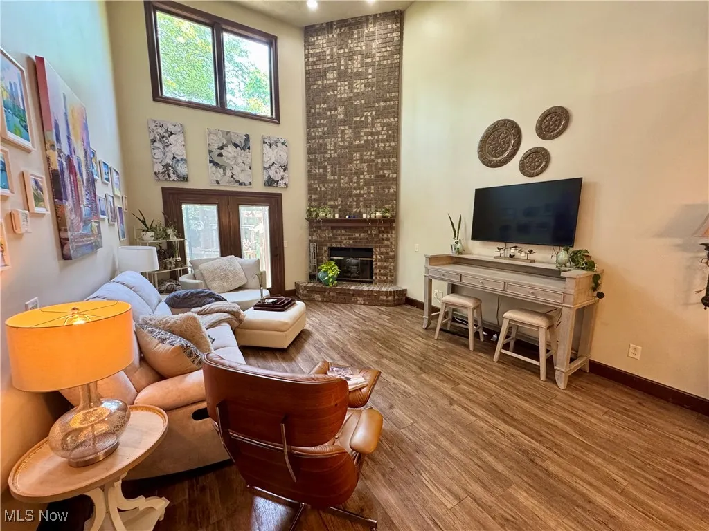 Living area featuring a brick fireplace, a high ceiling, and wood finished floors