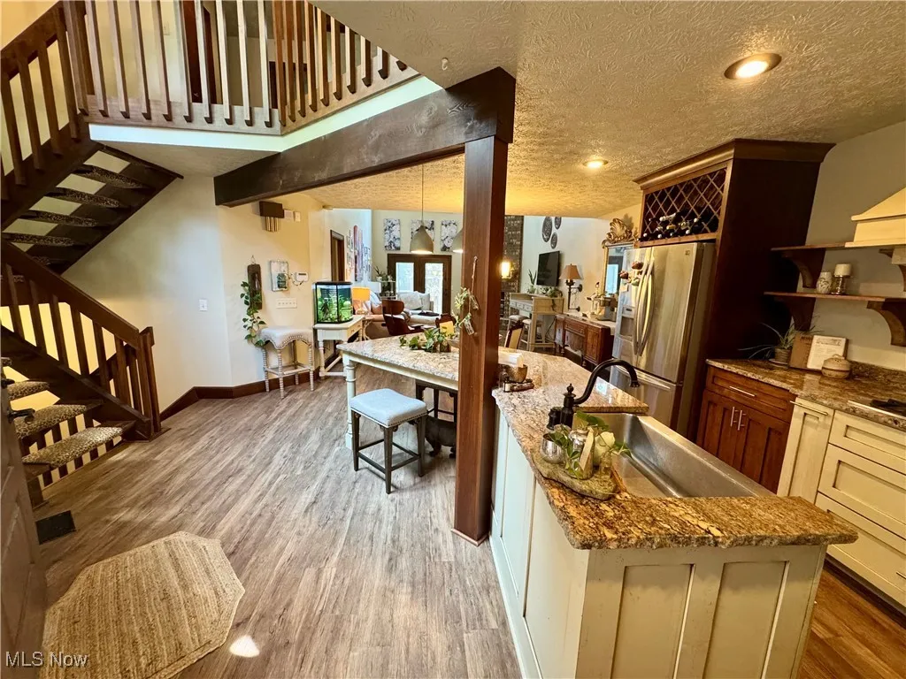Kitchen with stainless steel fridge with ice dispenser, light wood-style floors, open shelves, stone countertops, and a textured ceiling