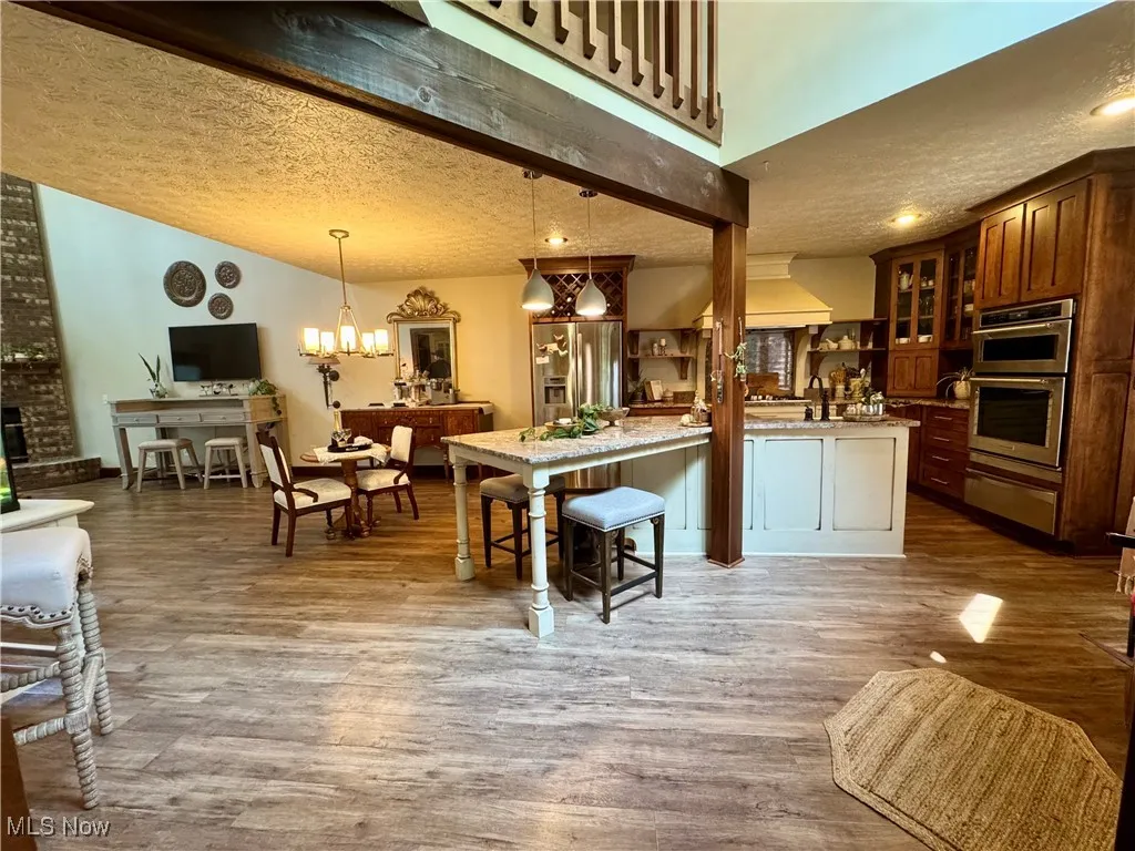 Kitchen with a textured ceiling, glass insert cabinets, a warming drawer, stainless steel appliances, and wood finished floors