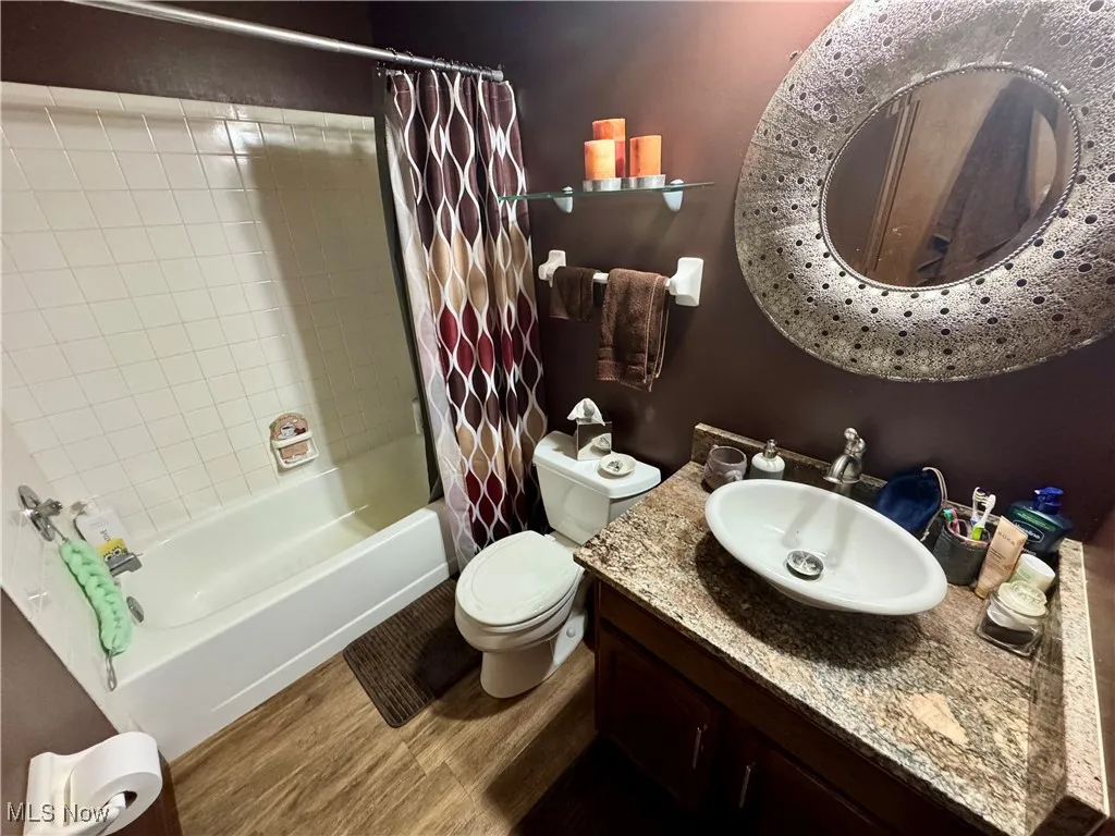 Bathroom featuring wood finished floors, shower / bath combo with shower curtain, and vanity