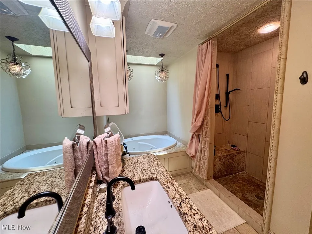 Full bath featuring a jetted tub, a stall shower, a textured ceiling, vanity, and tile patterned floors