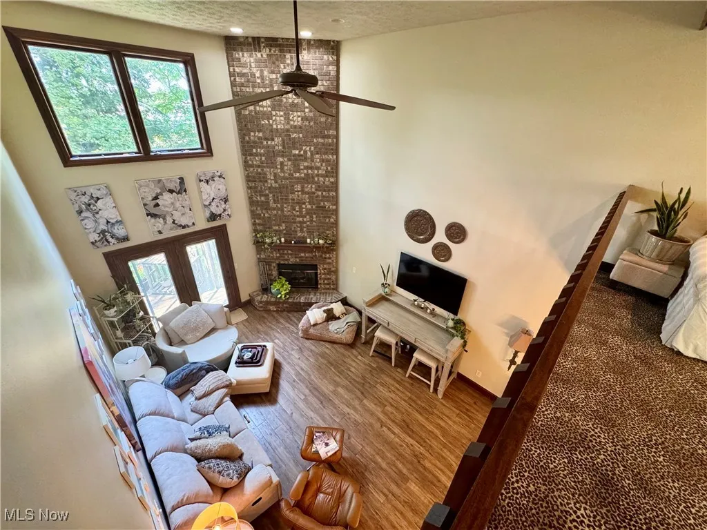 Living room with ceiling fan, wood finished floors, a brick fireplace, plenty of natural light, and a textured ceiling