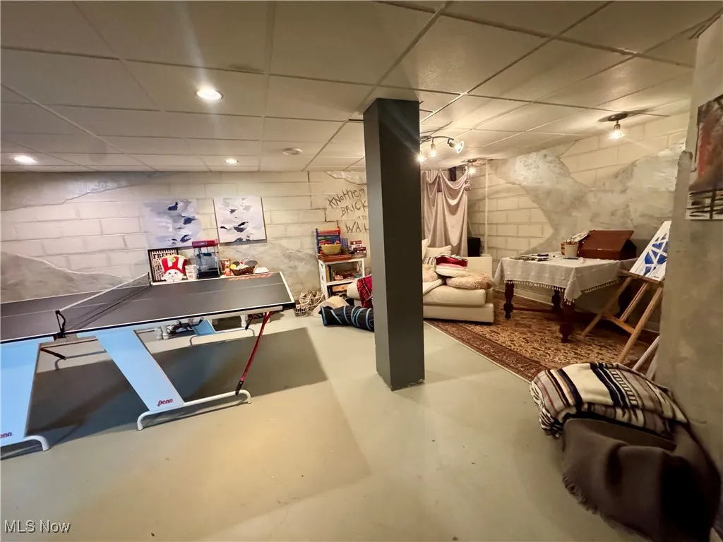Playroom featuring concrete flooring, concrete block wall, a drop ceiling, and recessed lighting