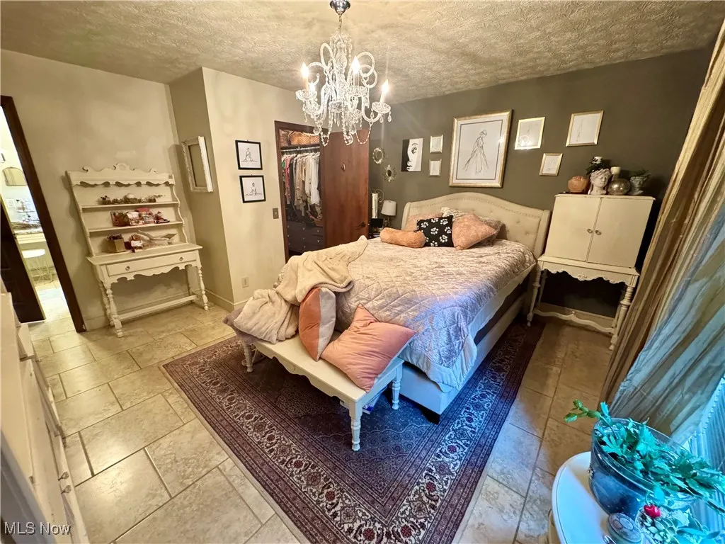 Bedroom featuring a textured ceiling, a chandelier, stone tile flooring, and a walk in closet