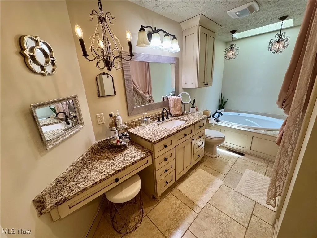 Full bath with a chandelier, vanity, a garden tub, and a textured ceiling
